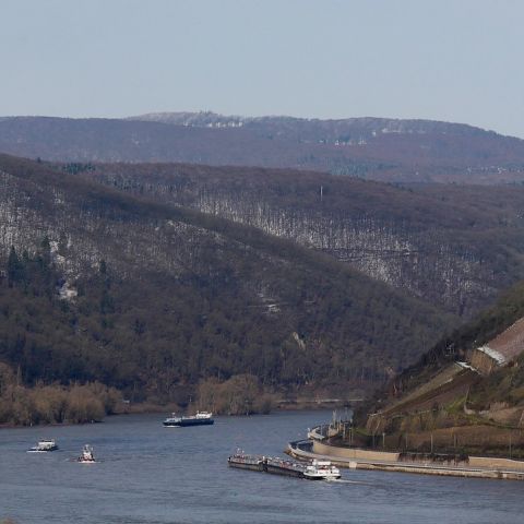 Panoramaansicht des Rheins bei Bingen mit historischen Burgen und Schiffen auf dem Wasser, umgeben von bewaldeten H?uuml;geln.